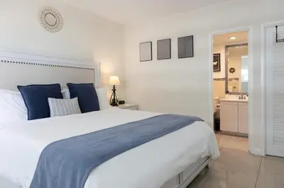 a white bedroom with a large bed and a bathroom at Beachfront 2 BR Apt Full Kitchen - No Resort Fee in Hollywood
