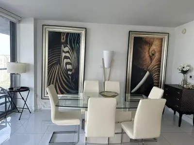 a dining room with a glass table and white chairs at Family Oriented Apartments with unbelievable views in Hallandale Beach