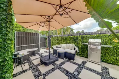 a patio with an umbrella and chairs and a grill at Mod Bungalow with Ultra-Private Outdoor Hang Space! in Miami Gardens