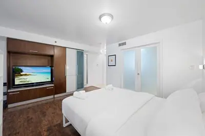 a white bedroom with a bed and a flat screen tv at Cozy Ocean Drive Studio - Roof top Pool and Bar in Miami Beach