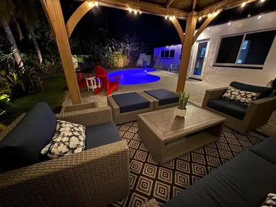 a patio with wicker furniture and a pool at night at NEW! Private Oasis with Heated Pool Minutes to Wilton Dr and the Beach in Fort Lauderdale