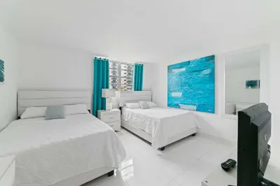 a white bedroom with two beds and a tv at Ocean Wind - Luxury Beachfront Condo with Pool & Gym in Hollywood