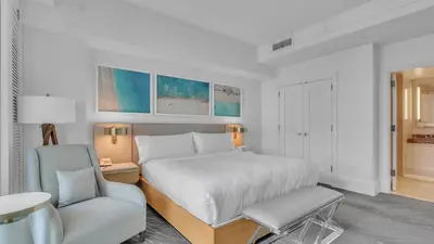 a white bedroom with a bed and a chair at Ritz-Carlton 2br 17th fl Penthouse Hotel Condo in Fort Lauderdale