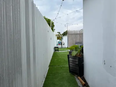 a small garden with green grass next to a white wall at Cottage with Hot Tub, Private Firepit, Entrance, Parking BBQ in Miami Gardens