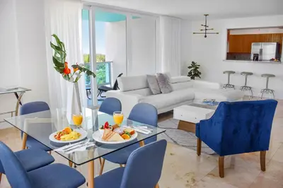 a living room with a glass table and blue chairs at Seacoast Suites on Miami Beach in Miami Beach