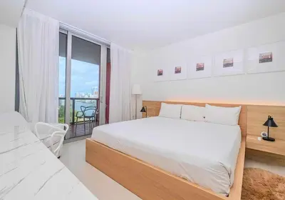 a white bedroom with a large bed and a balcony at Luxury Ocean View Apartment 1208 Hallandale Beach in Hallandale Beach