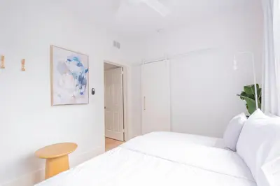 a white bedroom with a bed and a table at Designer 2BR Condo, 5 Mins to Sand, Free Parking in Hollywood