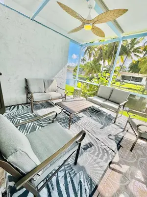 a patio with chairs and a table and a ceiling fan at 4bdrm Waterfront salt water Pool home with Outdoor theater Game Rm Make up vanities in every room Perfect for Game days and concerts trips to Miami Hard rock stadium and hotel 15 mins away in Miramar