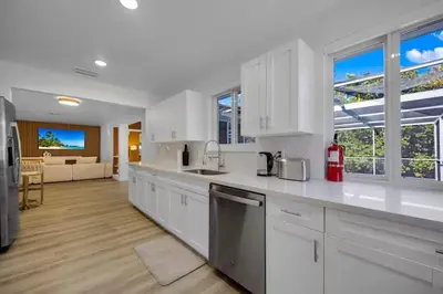 a kitchen with white cabinets and a living room at Hidden Miami Oasis Heated Pool and Games in Golden Glades