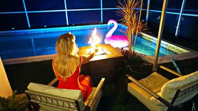 a woman sitting at a table with a fire in front of a pool at Hidden Miami Oasis Heated Pool and Games in Golden Glades