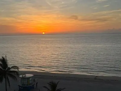 a sunset over the ocean with a building on the beach at Modern Beachfront Suite at Hollywood Broadwalk in Hollywood
