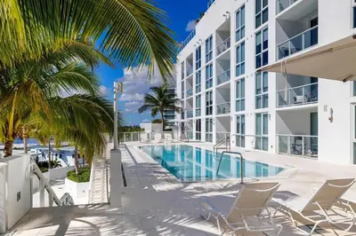 a resort pool with chairs and palm trees next to a building at Champagne at Tiffany's - Luxury Condo by the Beach in Fort Lauderdale