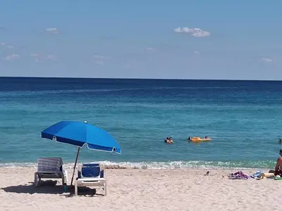 a beach with two chairs and an umbrella and people in the water at Estudios en las playa de Sunny Isles Beach in Sunny Isles Beach