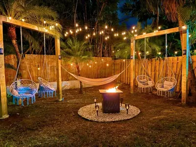 a hammock and chairs with a fire in a backyard at night at Friendly Fox Luxury Pool & Spa - Near DT & Beach home in Fort Lauderdale