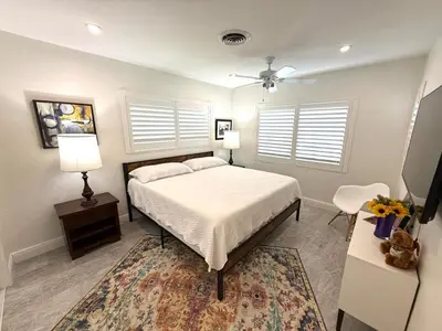 a bedroom with a bed and a table and two windows at The Pines Hideaway-Your Home Away from Home in Fort Lauderdale