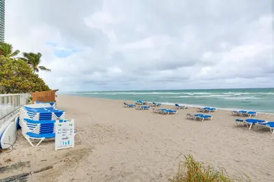 a beach with lounge chairs and the ocean at Oceanfront Resort Condo with Gym and Waterfront Pool! in Sunny Isles Beach