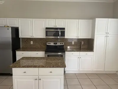 a kitchen with white cabinets and a stove and microwave at The Garden House in Miami Lakes in Miami Lakes