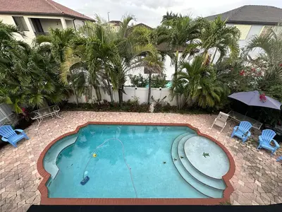 an empty swimming pool with an umbrella and chairs at The Miami Lakes Pool House in Miami Lakes