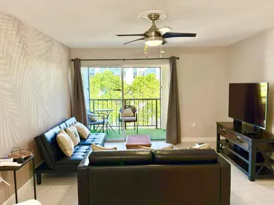 a living room with a couch and a flat screen tv at Modern 2 bedroom condo with heated pool, free parking spot at a 5 minute walk to the beach! in Sunny Isles Beach