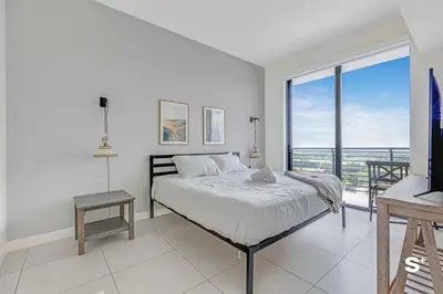 a white bedroom with a bed and a balcony at Doral 2BD Condo with Skyline Views and Fitness Center in Miami