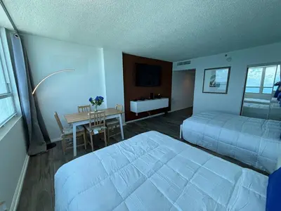 a bedroom with two beds and a table and a desk at 1701 - Studio Ocean Front Free Parking Pool in Miami Beach