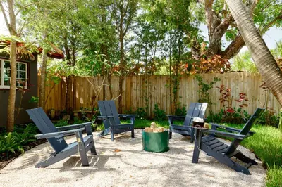 three chairs and a table in a backyard with a fence at Hacienda de Amor - Heated pool - Hot Tub - Firepit in Fort Lauderdale