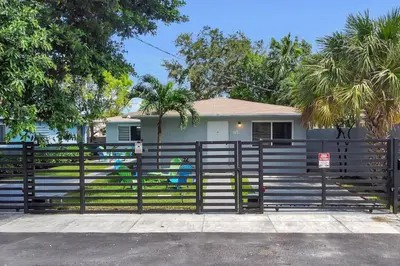 a fence in front of a house with palm trees at Stylish 2BR Retreat in Miamis Design District in Miami