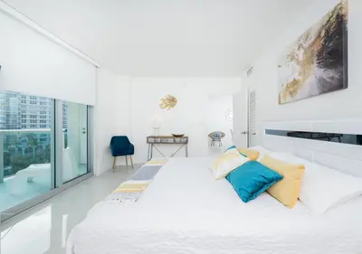 a white bedroom with a large bed with blue pillows at Hollywood Beachfront 2-Bedroom Condo with Ocean Views in Hollywood