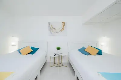 two beds in a white room with blue and yellow pillows at Hollywood Beachfront 2-Bedroom Condo with Ocean Views in Hollywood