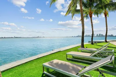 a row of lawn chairs and palm trees next to the water at Villa Tropique in Miami Beach