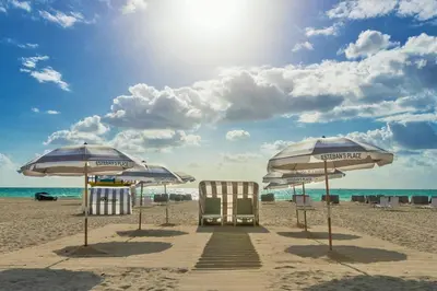 two beach chairs and umbrellas on a sandy beach at Henrosa Hotel in Miami Beach