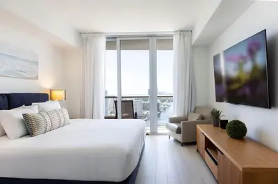 a white bedroom with a large bed and a living room at 1 BR Full Kitchen- Pool Gym Beach 29th floor in Hallandale Beach
