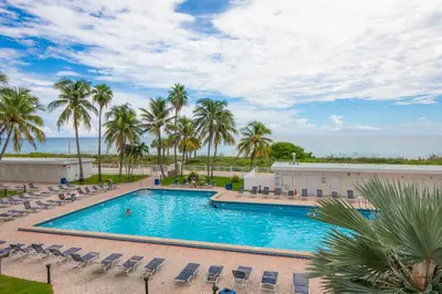 a pool with chairs and palm trees and the ocean at Casablanca Residences Miami Beach in Miami Beach