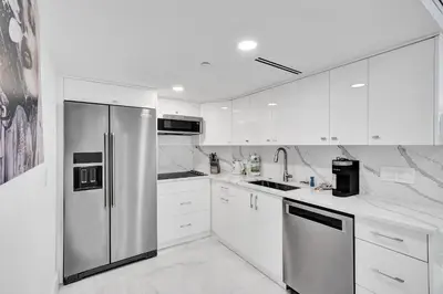 a kitchen with white cabinets and a stainless steel refrigerator at Oceanfront Escape with Resort Amenities Gym Pools and Sauna 1408 in Miami Beach