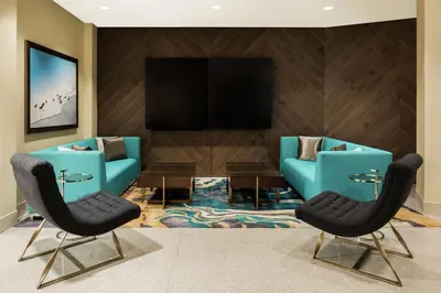 a living room with two blue chairs and a flat screen tv at Hilton Garden Inn Miami Dolphin Mall in Miami