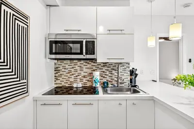 a white kitchen with a microwave and a sink at Chic Modern Studio with Queen Bed in Fort Lauderdale
