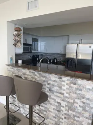 a kitchen with a counter with chairs and appliances at Luxurious 2BD Condo with Direct Ocean Views & Resort Pool in Sunny Isles in Sunny Isles Beach