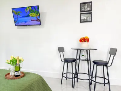 a room with two tables and two stools and a table with flowers at Luxury Suite Studio with Kitchen & Spa Shower in Miramar