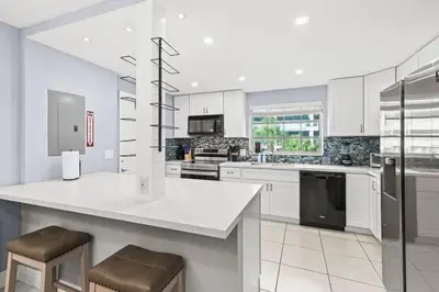 a white kitchen with a counter and stools in it at Beach Pool & Las Olas Getaway Fort Lauderdale in Fort Lauderdale