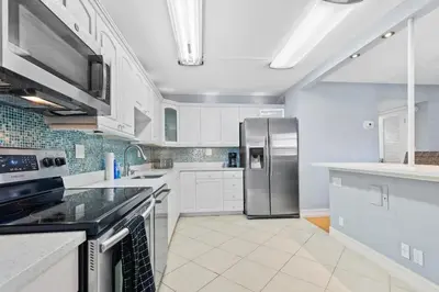 a kitchen with white cabinets and a stainless steel refrigerator at Beachside Las Olas Getaway Oasis with Pool in Fort Lauderdale