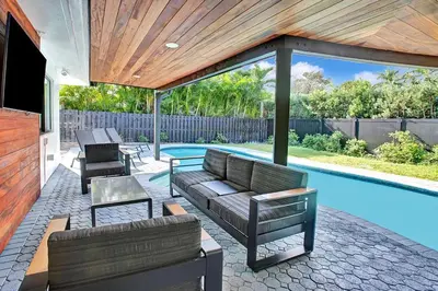 a patio with a couch and chairs next to a swimming pool at Coral Lane by Rove Travel - Home with Pool & BBQ in Fort Lauderdale