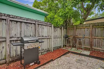 a backyard with a grill and two stools next to a fence at Casa Sol A in Fort Lauderdale