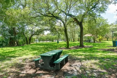 a green park bench in a park with trees at Beach Oasis Heated Pool, Gazebo, Hot Tub in Fort Lauderdale