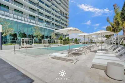 a pool with chairs and umbrellas next to a building at Coastal Apartment - Pool & Breezy Balcony in Miami Beach