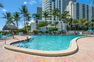 a swimming pool at a resort with palm trees and buildings at Family-Friendly Beach Condo Steps to the Ocean- 9th floor in Hollywood Beach