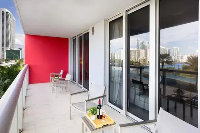 an apartment balcony with a red wall and chairs at Amazing 2 BR Apartment Pool & Near Beach in Hallandale Beach
