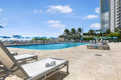 a swimming pool with chairs and blue umbrellas at Beachfront Studio with Resort Access STR-02630 in Sunny Isles Beach