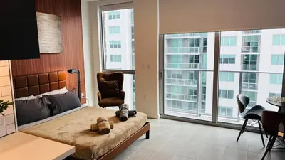 a bedroom with a bed and a chair and a large window at Skyline Studio Workspace & Rooftop Pool in Miami