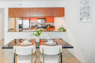 a dining room with a glass table and white chairs at Luxury 2BD Condo | Sauna, Pool & Resort Access in Miami