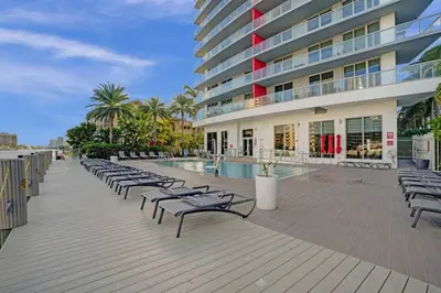 a row of chaise lounge chairs on a boardwalk near a building at Ocean View 3 BDR Condo Pool Gym Private Balcony in Hallandale Beach
